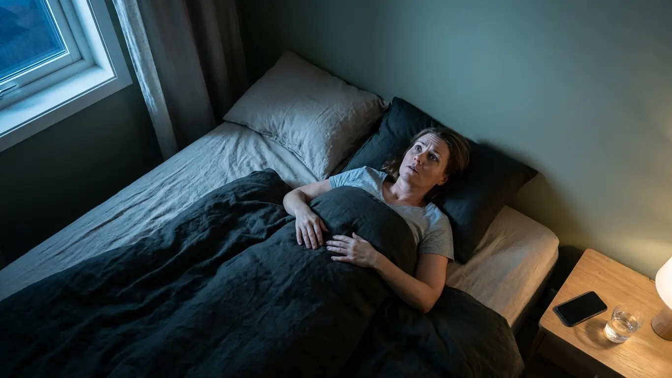 Femme éveillée dans son lit la nuit, les yeux fixés au plafond, absorbée par des pensées qui tournent en boucle